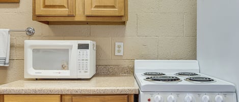 A kitchen with a white microwave, a stove with four burners, wooden cabinets, and a white countertop.