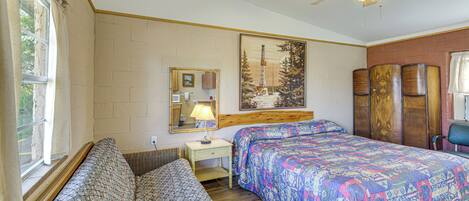 A bedroom with two beds, a wooden headboard, a ceiling fan, a window with curtains, a bedside table with a lamp, and a framed picture on the wall.