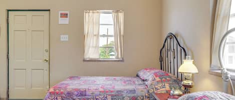 A bedroom with two beds, a window with curtains, a bedside lamp, and a door.
