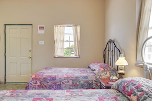 Un dormitorio con dos camas, una ventana con cortinas, una lámpara de noche y una puerta.