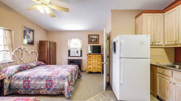 A compact room with a bed, a refrigerator, a television, and a ceiling fan.