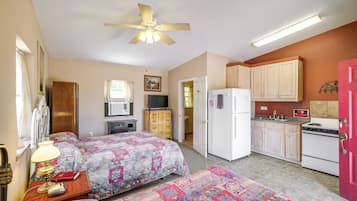 Une chambre de taille modeste, équipée de deux lits, d’un coin cuisine, d’un ventilateur de plafond et d’une télévision.