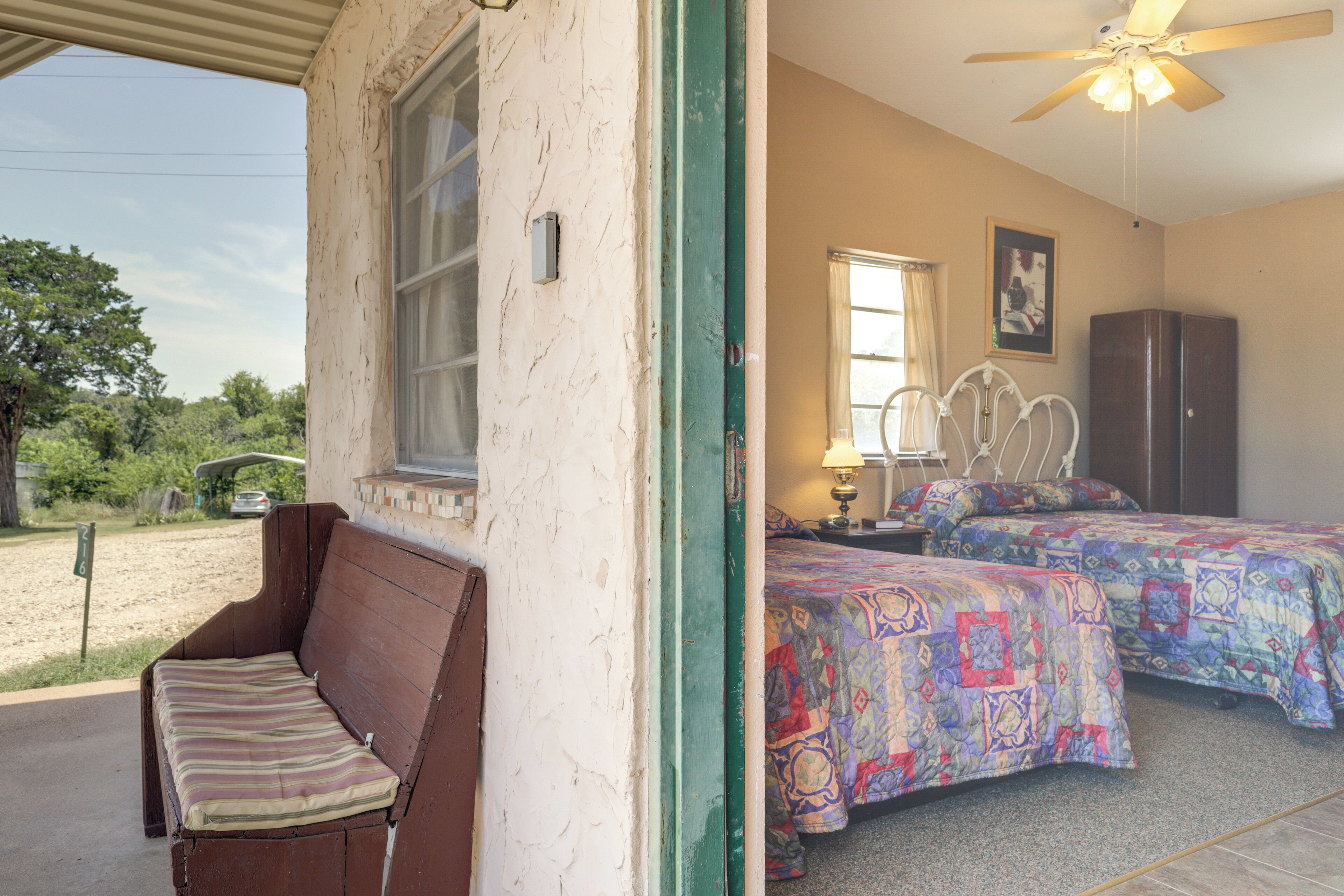 A bedroom with two beds, a wooden bench, a ceiling fan, and a window with curtains.