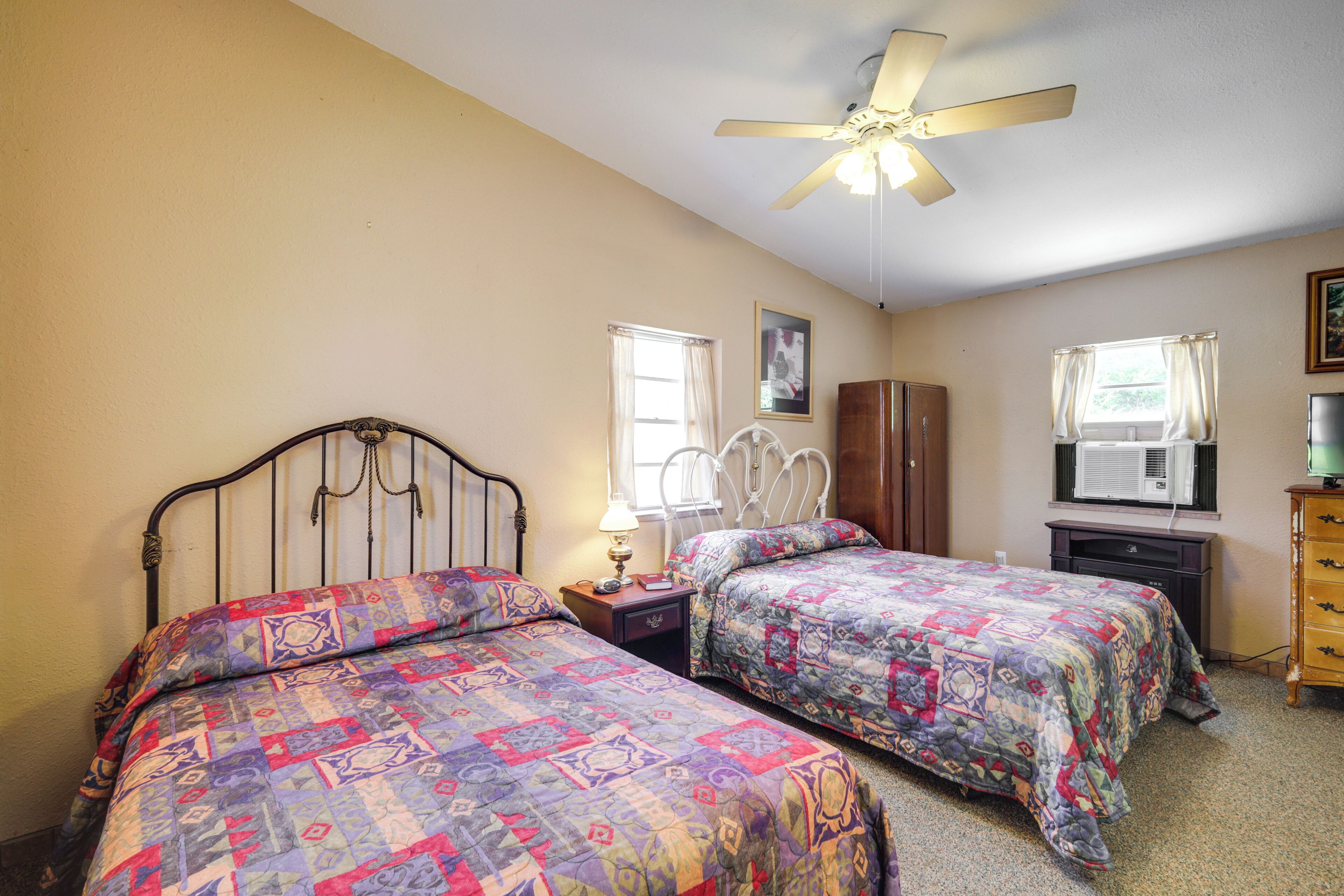 A bedroom with two beds, a ceiling fan, a dresser, and a window with curtains.