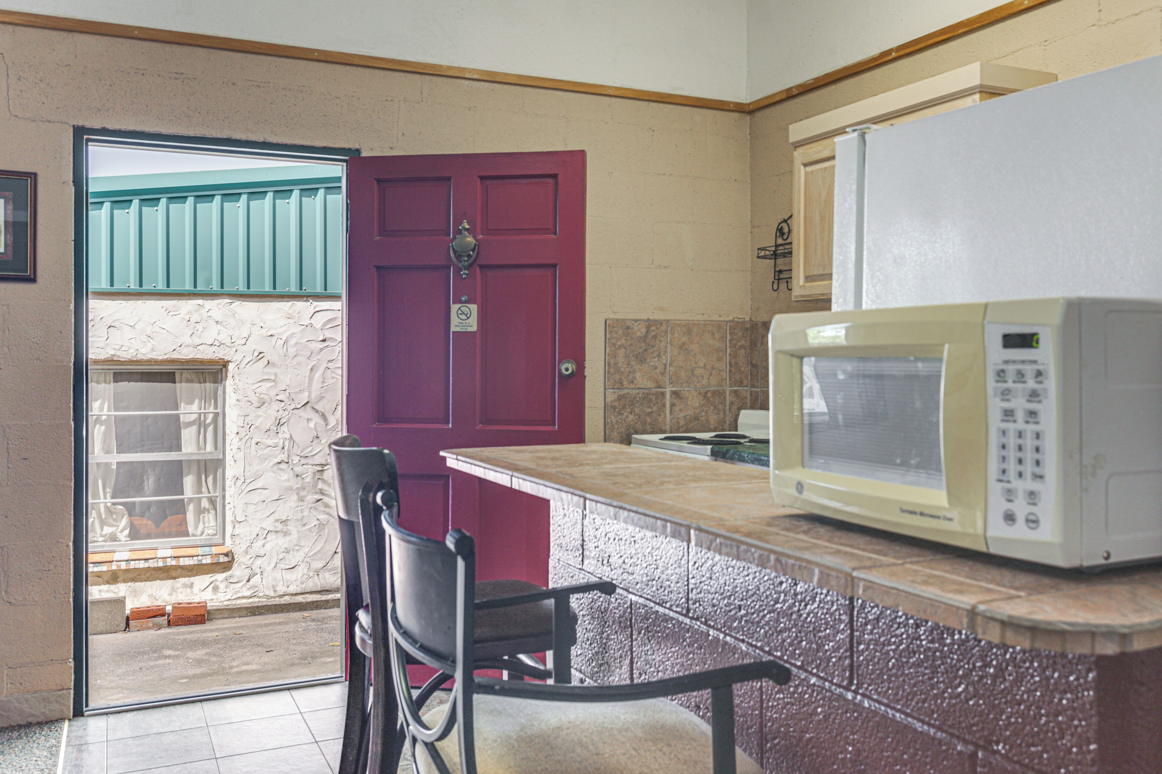 A kitchen with a red door, a white microwave, and a chair.
