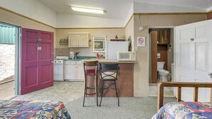 Eine kleine Küche mit grundlegender Ausstattung, ein Essbereich mit einem Stuhl und ein kleines Schlafzimmer mit einem Bett.