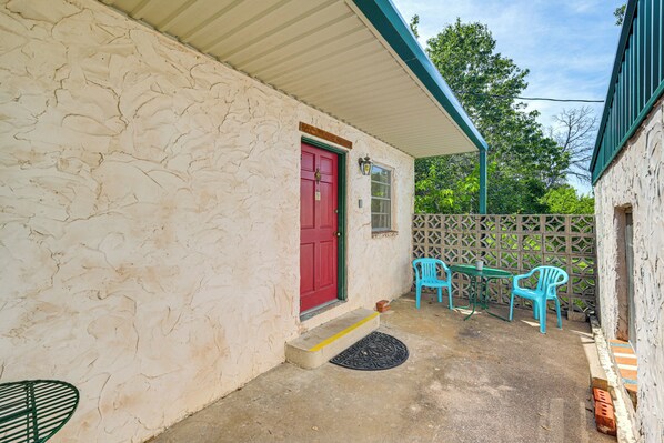 A stone building with a red door, a covered porch, and two blue plastic chairs. - Patio & Trail Access: Lake Whitney Studio! (Whitney)