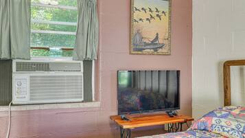 A room with a bed, a television on a wooden stand, an air conditioning unit, and a painting on the wall.