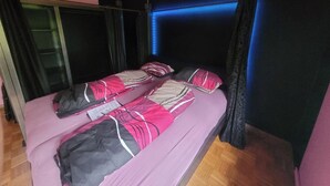 Ein Bett mit einer pink-schwarz gestreiften Tagesdecke, ein Holzboden und ein Fenster mit Vorhängen.