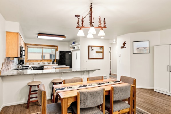 A modern kitchen with a central island, wooden bar stools, and a dining table with patterned runners. - Top Floor, 1 Block From Main, Peak 9, 4 OClock Run (Breckenridge)