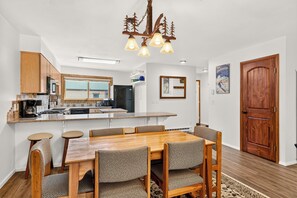 A modern kitchen with a central island, wooden dining table with chairs, and a chandelier.