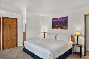 A hotel room with a large bed, two bedside lamps, a night sky view, and a wooden door.