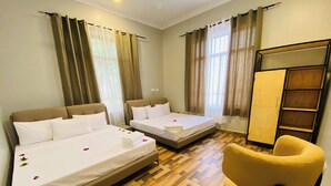 A hotel room with two beds, a wooden floor, a yellow armchair, and a wardrobe.