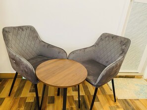 Two grey upholstered chairs with a quilted backrest and a round wooden table between them.