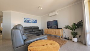 Un salon moderne avec un canapé en cuir, une table basse en bois, un téléviseur à écran plat posé sur un meuble en bois et une grande plante en pot.
