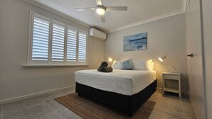 Une chambre à coucher avec un lit, un ventilateur de plafond, un tableau et une table de chevet.