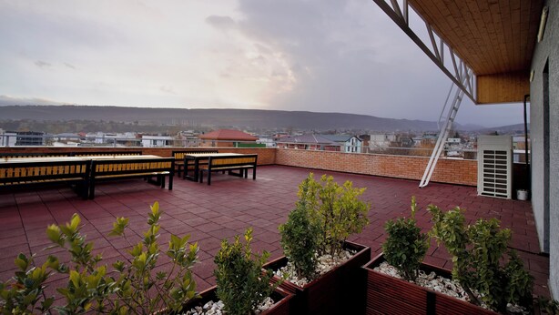 Terraço no telhado com um banco de madeira, uma mesa e plantas em vasos.