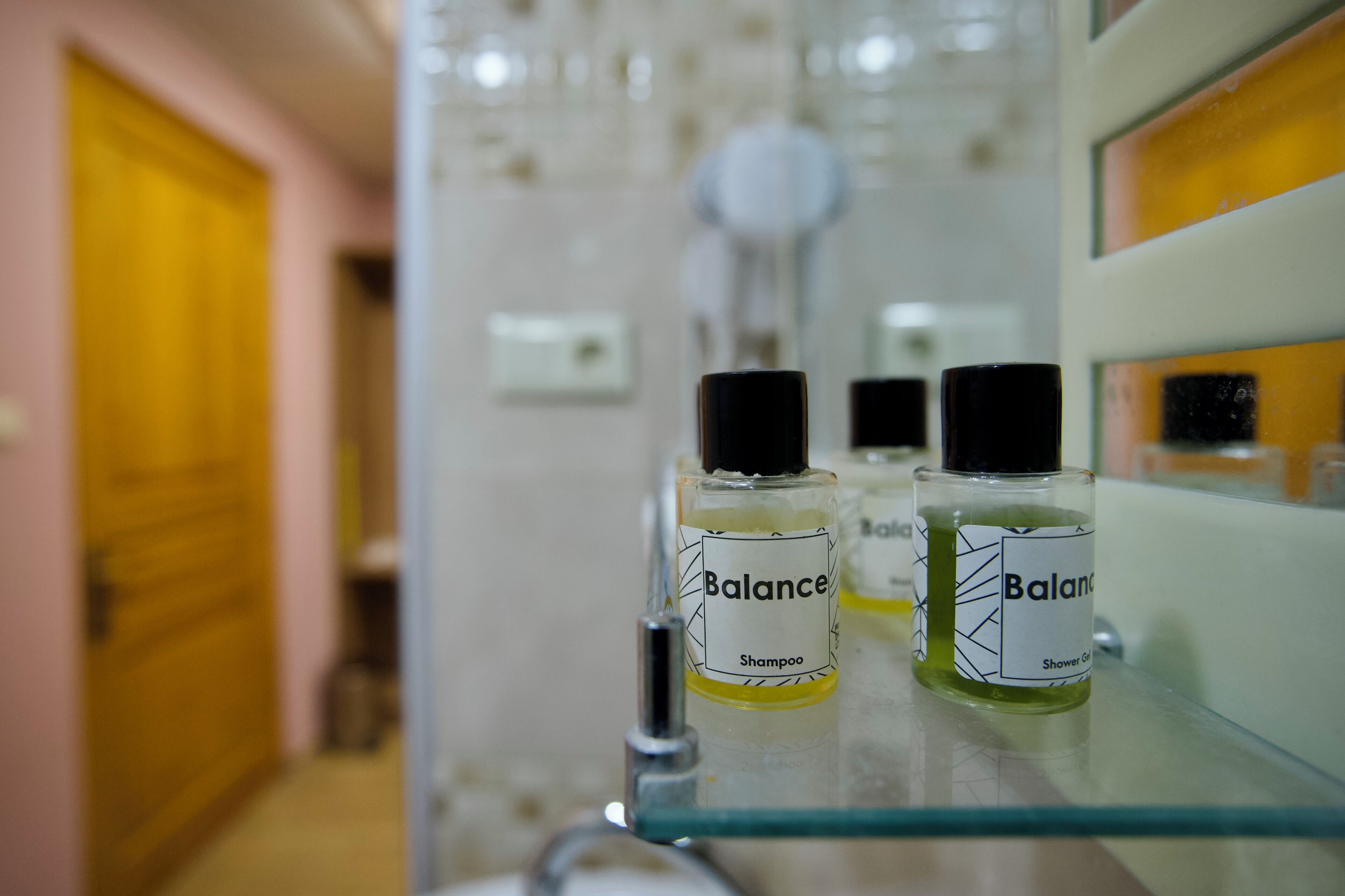 A bathroom with a glass shelf holding two bottles of Balance shampoo and shower gel.