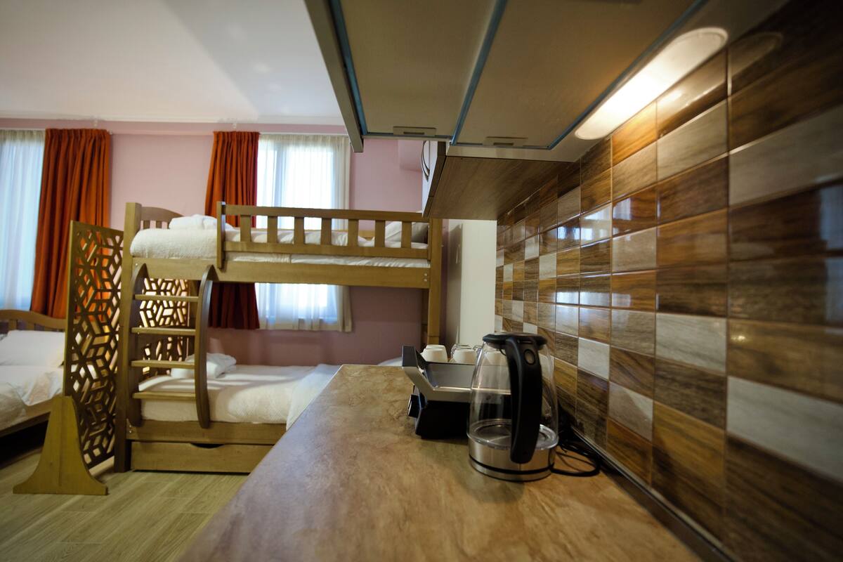 Quarto com beliche, escada de madeira, cafeteira e parede revestida com azulejos.