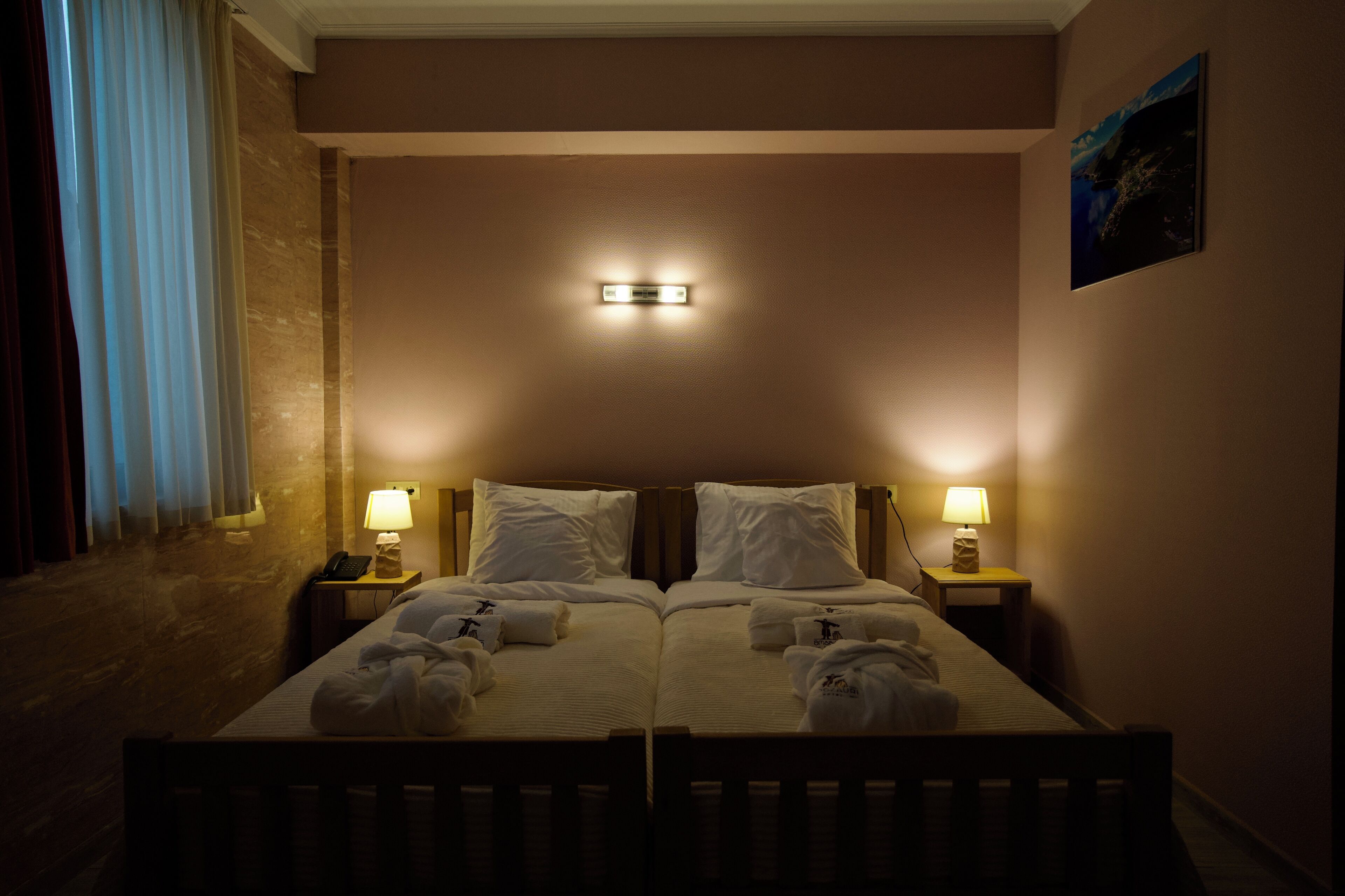 Ein Doppelbett mit zwei Nachttischen, jeder Tisch mit einer Lampe, in einem schwach beleuchteten Zimmer mit einer Leuchte über dem Bett.