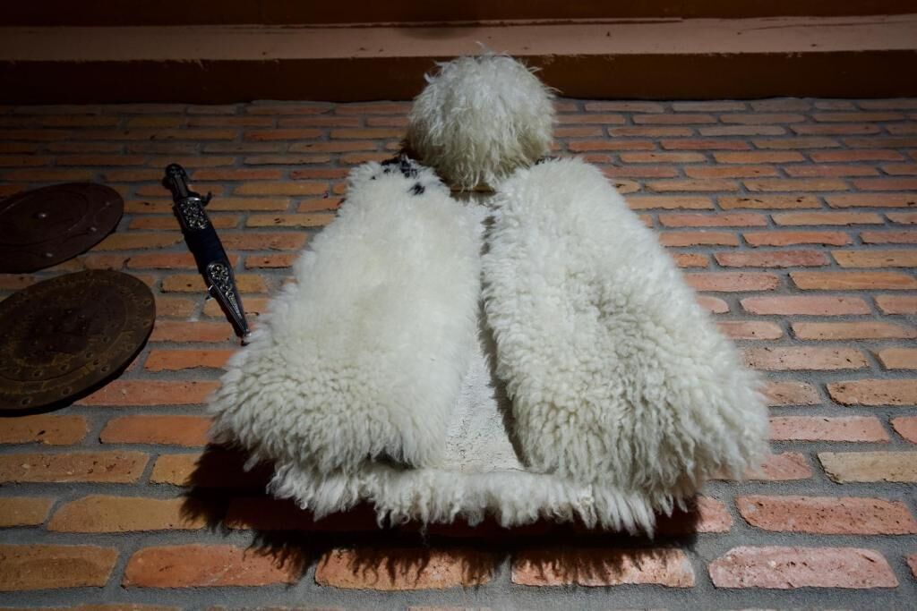 A rustic room with a brick floor, a fur-covered bench, and a sword leaning against the wall.