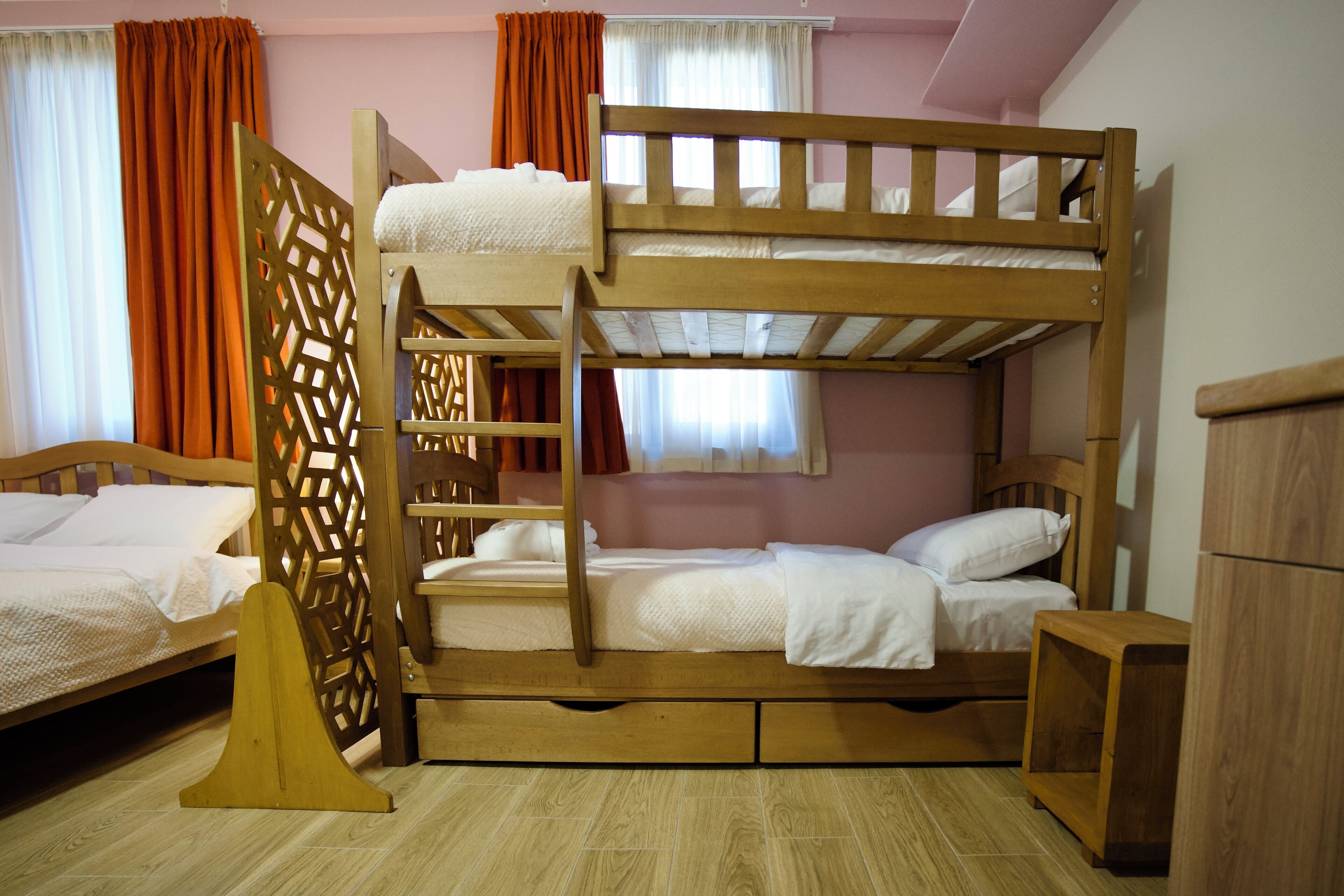 A bunk bed room with two beds, a wooden wardrobe, and a small table.