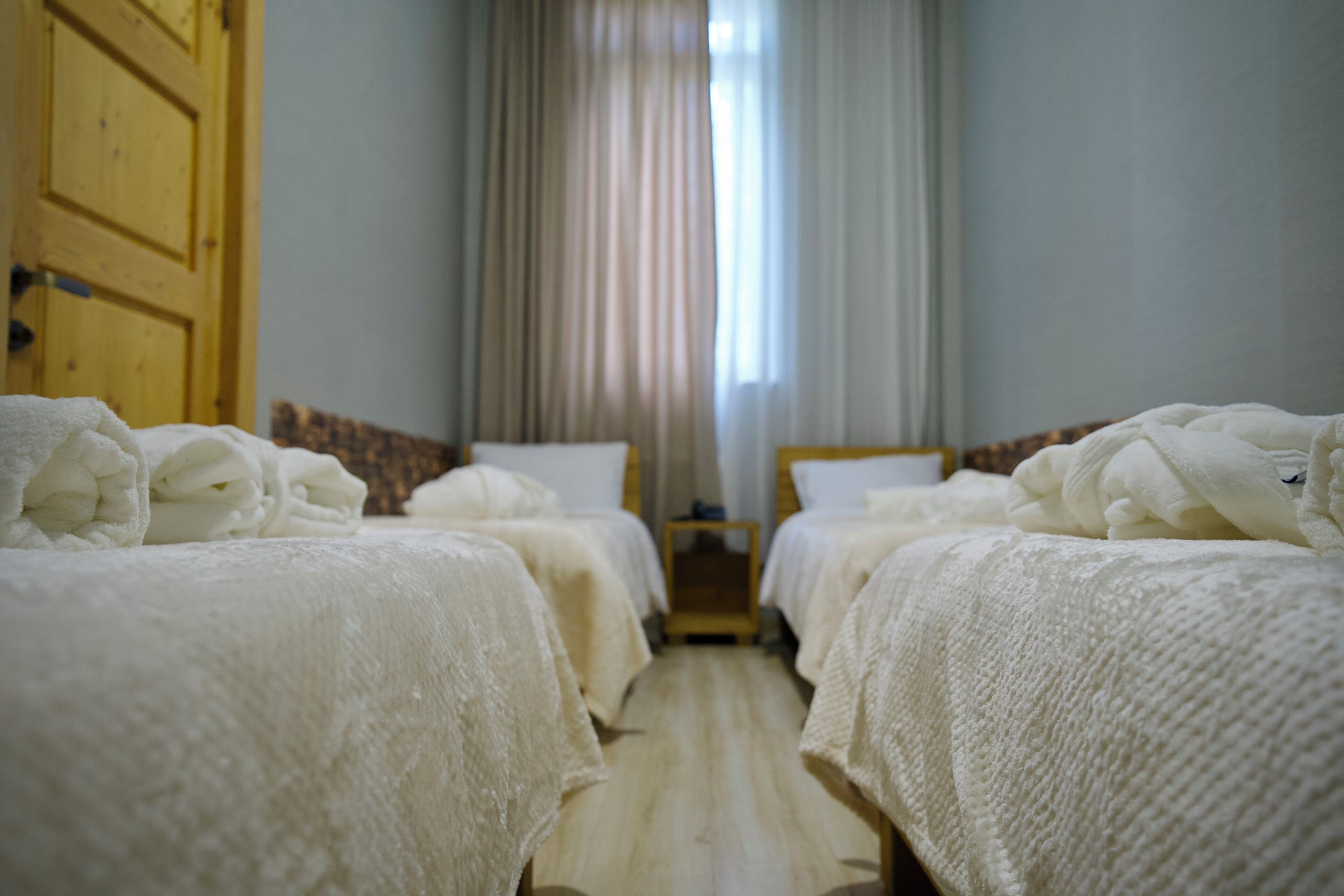 A hotel room with two beds, a wooden door, and a window with curtains.