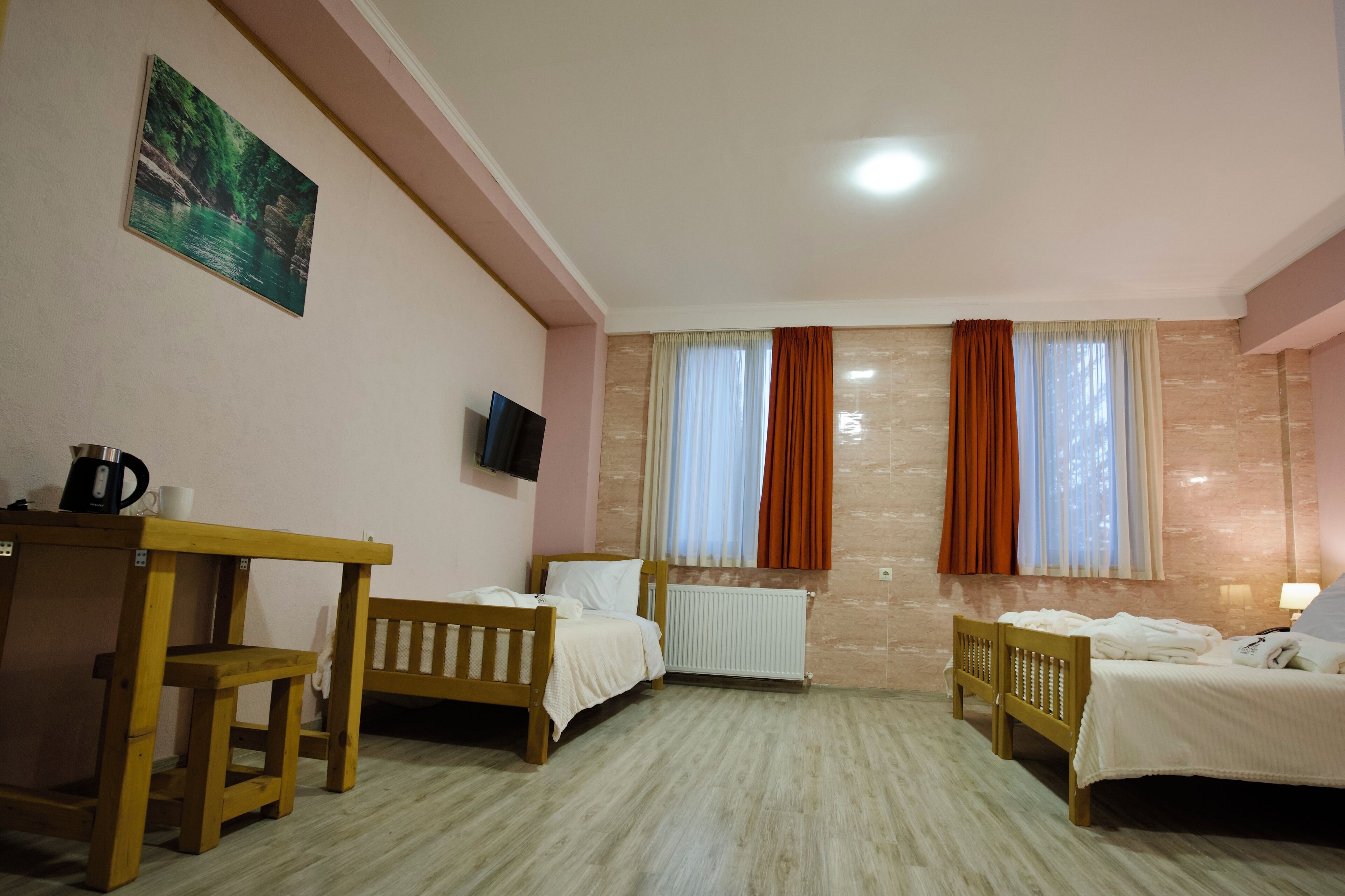 A hotel room with two single beds, a wooden desk with a chair, a television, and a painting on the wall.