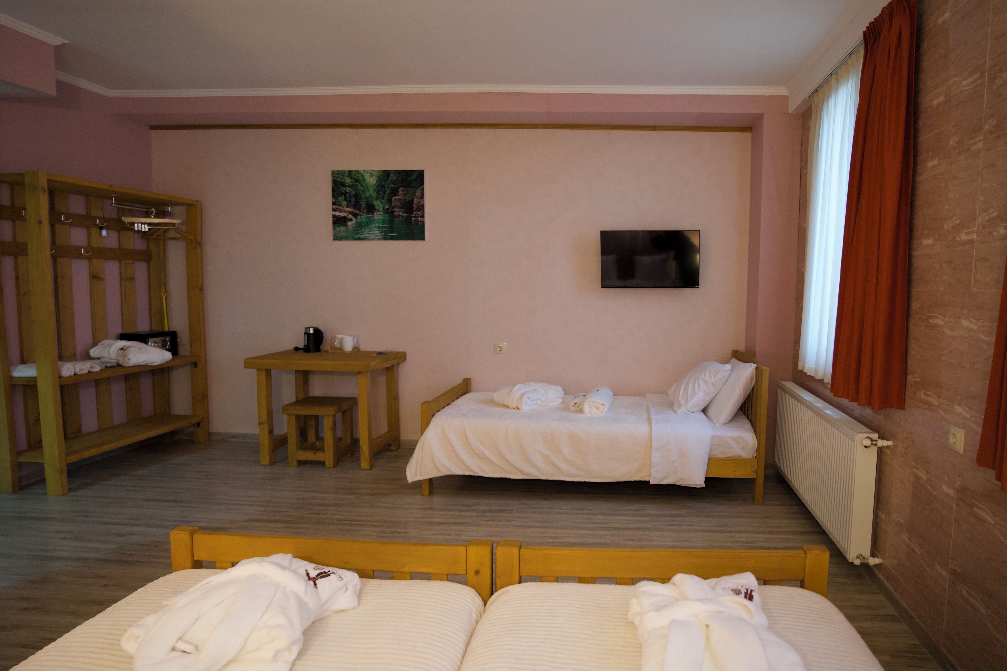 A room with two beds, a small table, a TV, and a wooden shelf with towels.
