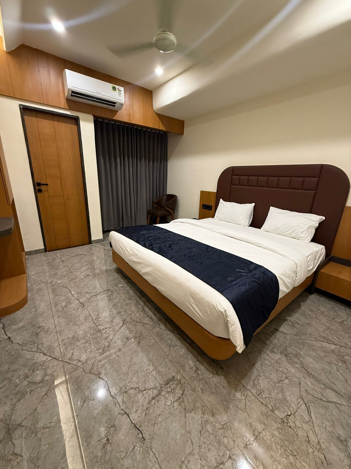 Een moderne hotelkamer met een marmeren vloer, een groot bed met hoofdeinde, een airconditioningapparaat en een houten deur.