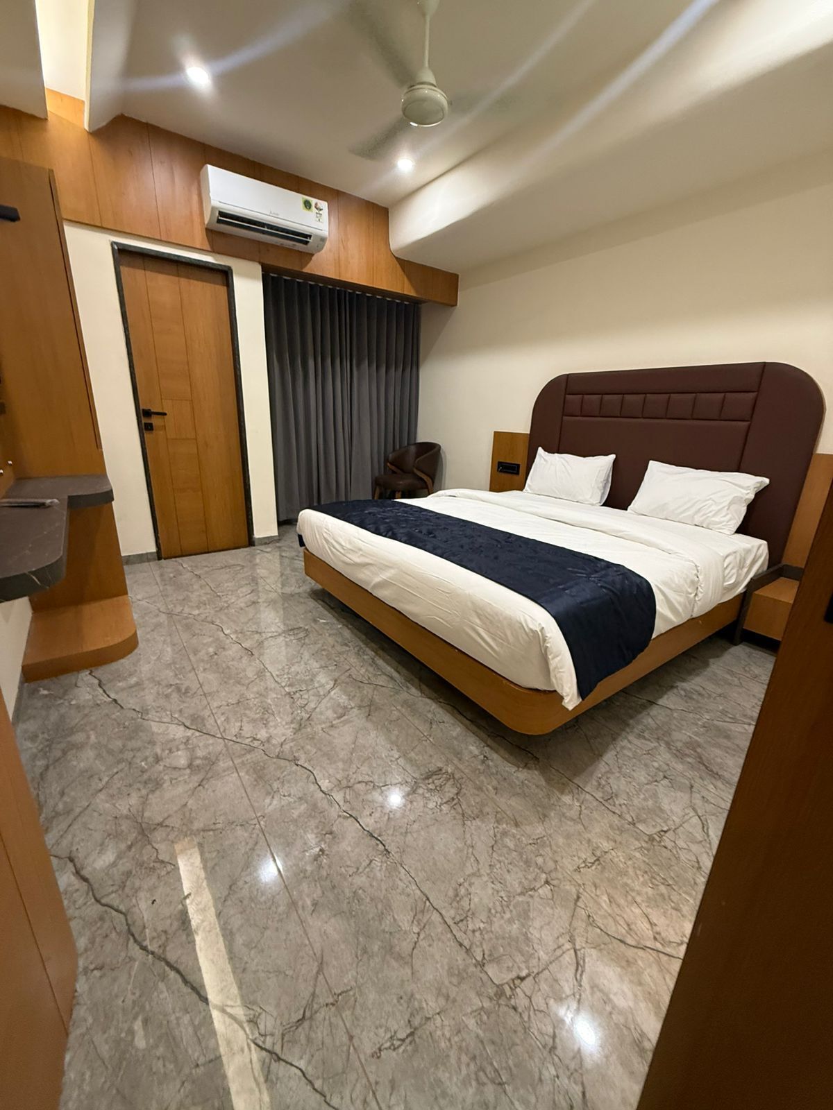 A hotel room with a bed, a wooden door, an air conditioning unit, and a marble floor.