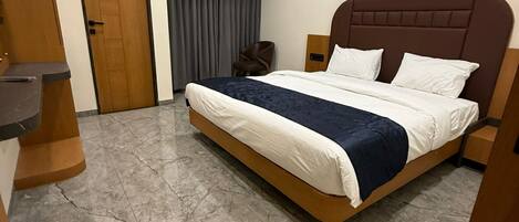 A hotel room with a bed, a wooden door, an air conditioning unit, and a marble floor.