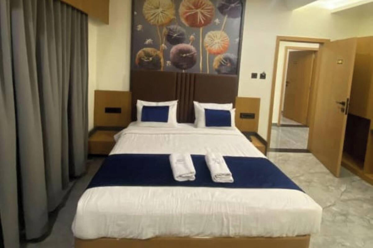 Quarto de hotel com uma cama grande, ventoinha no teto, um quadro na parede e uma porta que dá para outro cômodo.