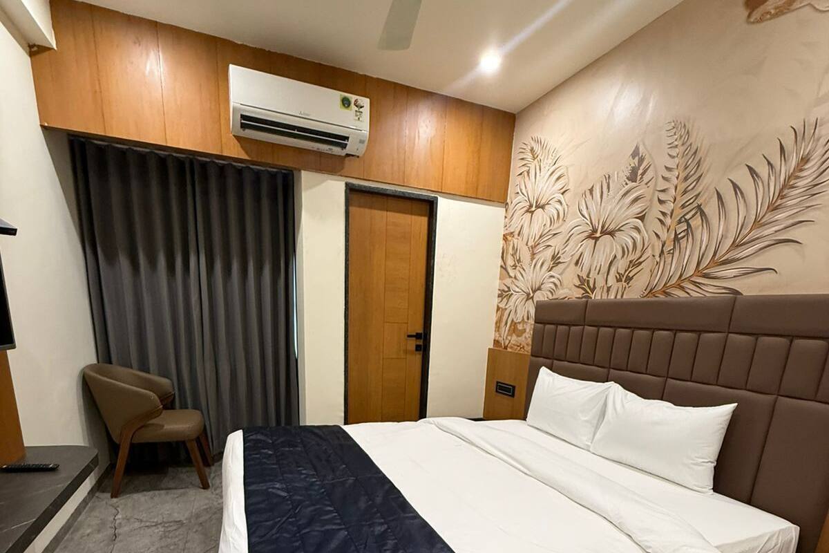Quarto de hotel com cama, poltrona, escrivaninha, ar condicionado e porta.
