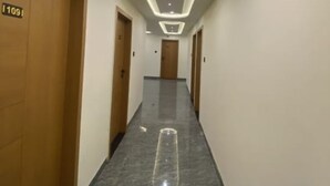 Un couloir d’hôtel moderne avec un sol en marbre, des portes en bois et un éclairage encastré au plafond.