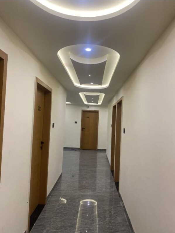 Un pasillo con un diseño moderno en el techo, puertas de madera y suelo de mármol.