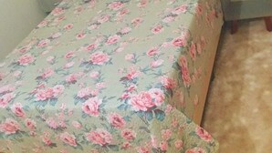 Un lit avec une couvre-lit à motifs floraux, une tête de lit et une table de chevet avec une lampe.