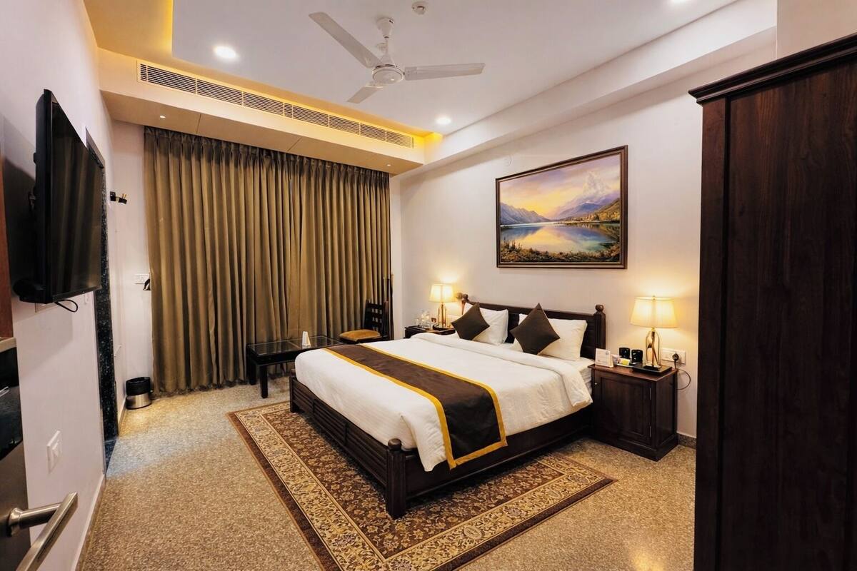 Une chambre d’hôtel avec un lit, des lampes de chevet, un tableau, un ventilateur de plafond et un téléviseur.
