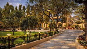 A paved pathway lined with trees and potted plants, leading to a building with multiple windows and balconies. - Daksh The Fateh Retreat - Udaipur (Udaipur)