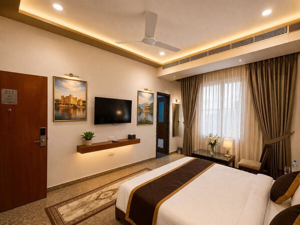 A hotel room with a bed, a TV, a ceiling fan, a desk with a lamp, and a window with curtains. - Daksh The Fateh Retreat - Udaipur (Udaipur)