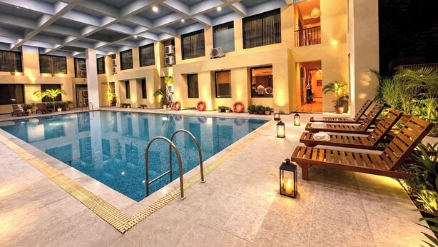 An indoor swimming pool with lounge chairs and potted plants, surrounded by a building with balconies and air conditioning units. - Daksh The Fateh Retreat - Udaipur (Udaipur)