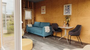 A modern room with a blue sofa, two chairs, a small table, and a window. - Solglimt 2 Pers Holiday Home With Stunning Views (Callantsoog)