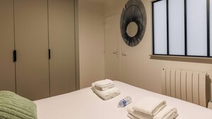 A hotel room with a bed, a radiator, a window with blinds, a wall-mounted mirror, and a wardrobe. - Cosy Apartment - 1br/4p - Near Nation (Paris)