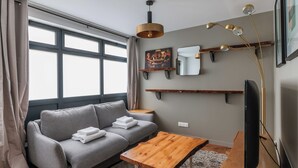A modern living room with a grey sofa, a wooden coffee table, a flat-screen TV, and a large window with curtains. - Cosy Apartment - 1br/4p - Near Nation (Paris)