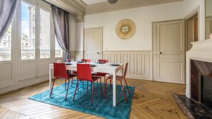 Un comedor con una mesa blanca, sillas rojas, un tapete azul y una chimenea.