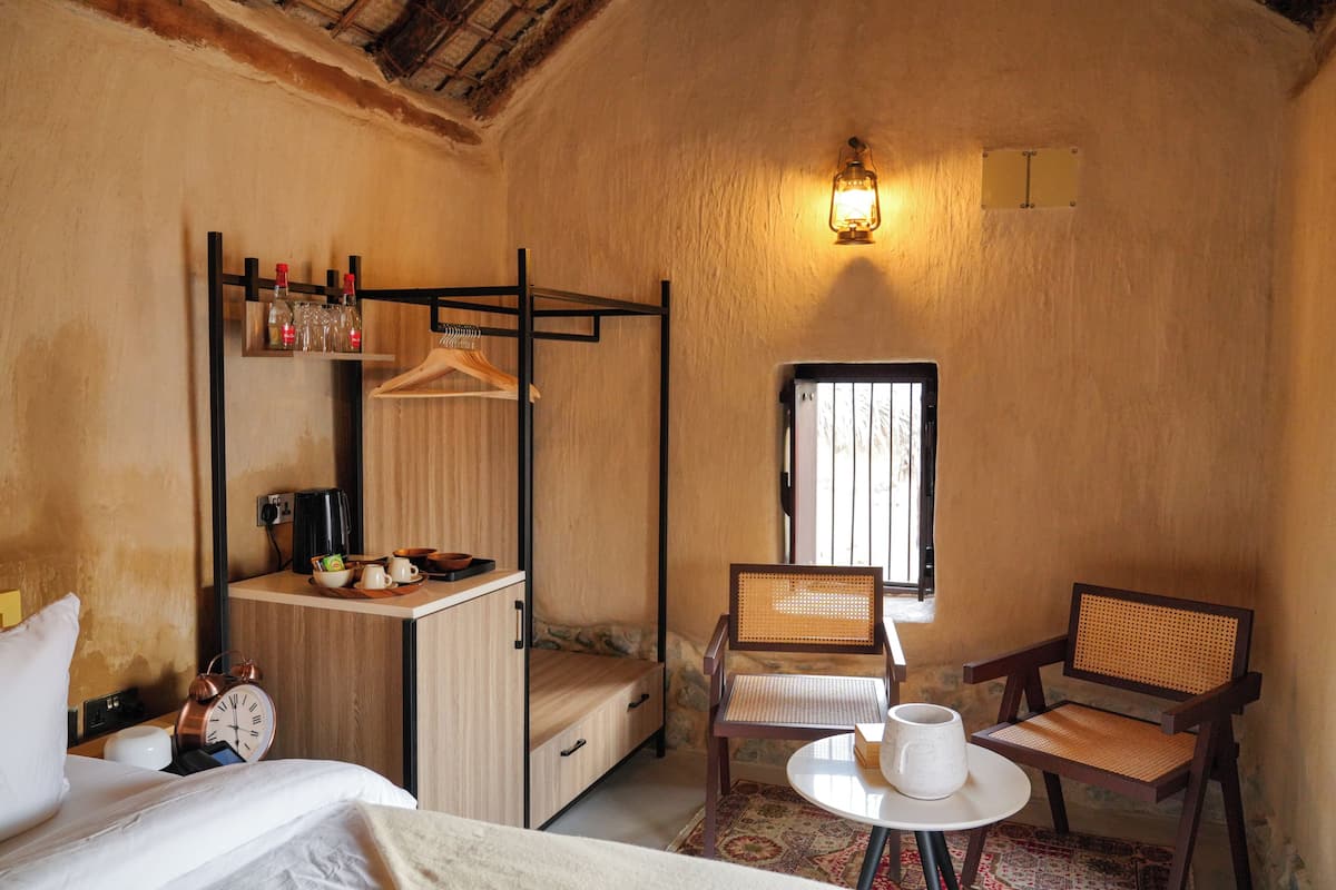 A room with a bunk bed, a small table with a cup, two wicker chairs, a clock, and a wall-mounted shelf with bottles.
