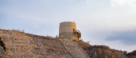 A historic tower with a circular base and a balcony, surrounded by dry grass.