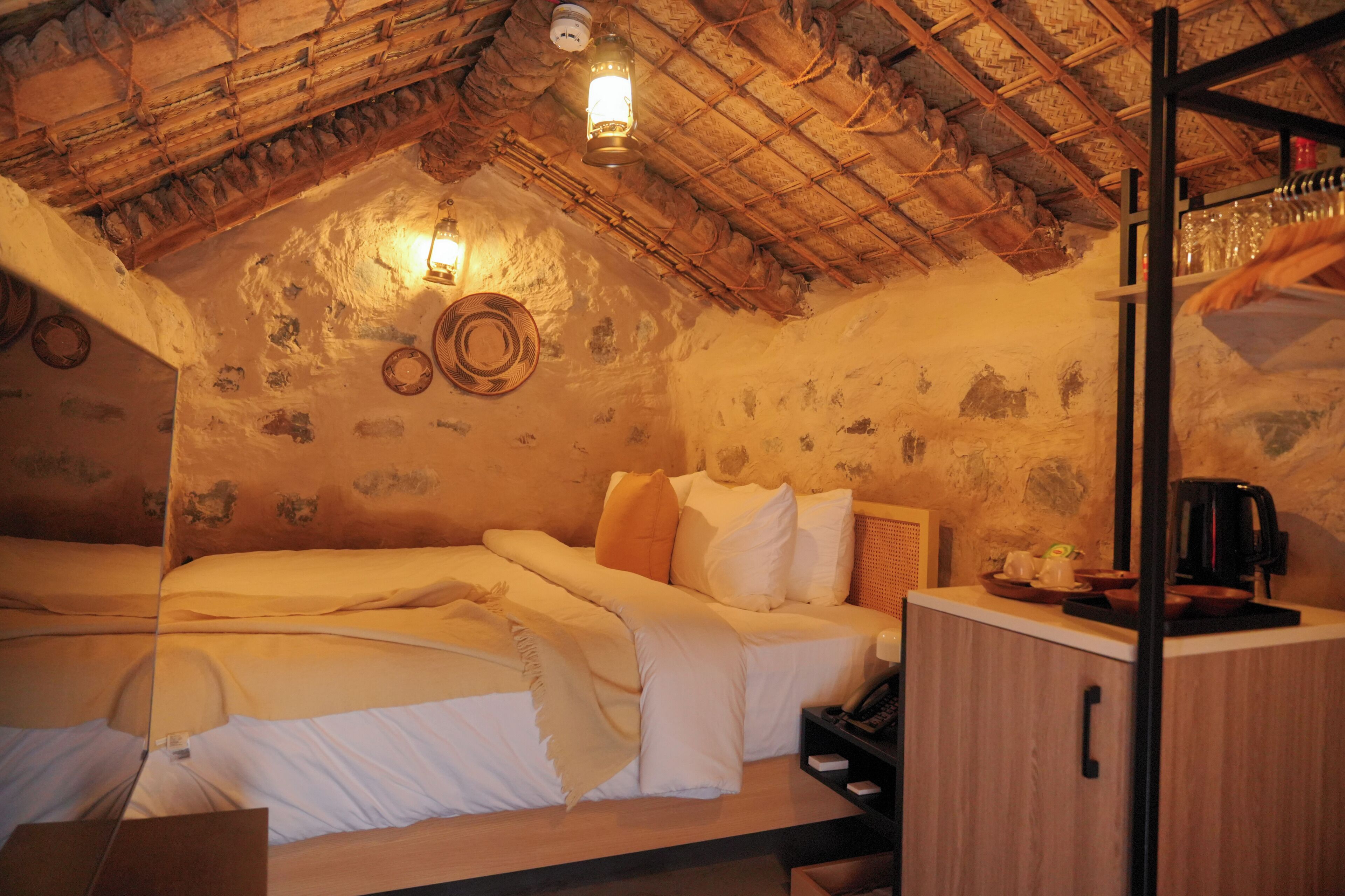 A rustic room with a wooden ceiling, a bed with white bedding, a small wooden cabinet, and a lantern-style light fixture.