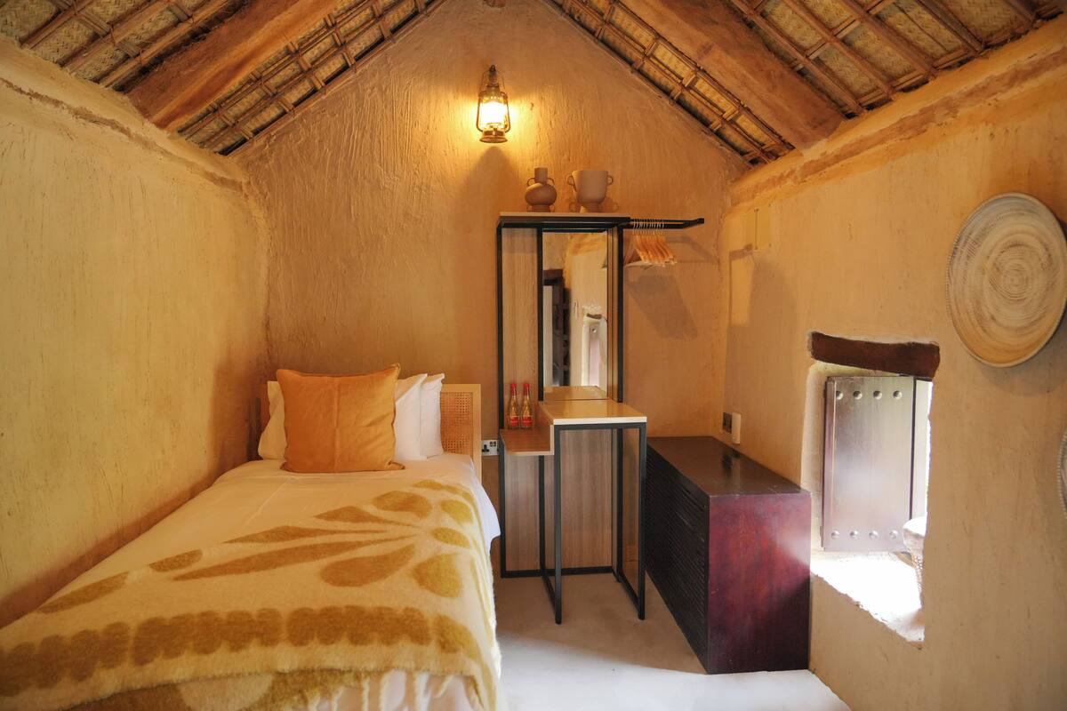 A cozy room with a bed, a small desk, a mirror, and a window.