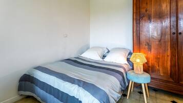 Een slaapkamer met een bed, kussens, een bedlampje, een houten garderobe en een klein krukje.